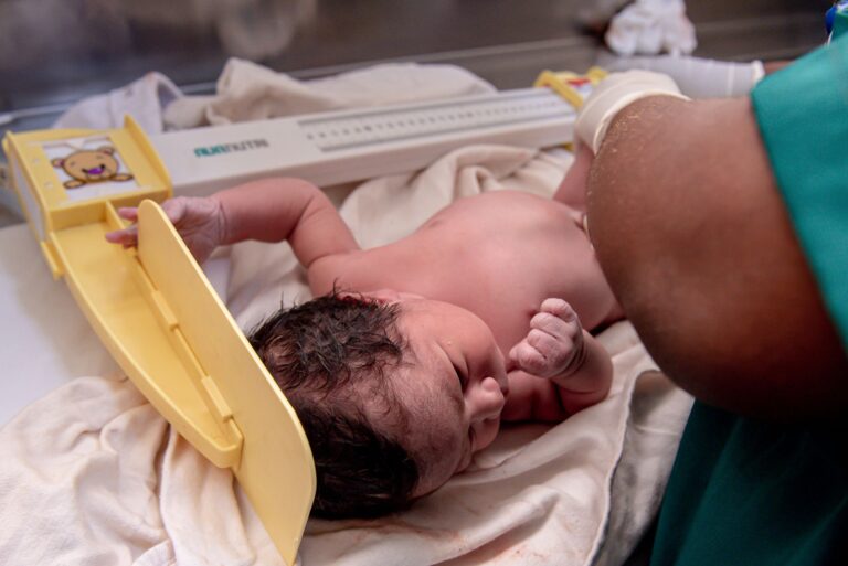 a newborn baby is weighed by a healthcare worker in a hospital setting. captured close-up.