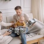 a happy family with a baby opening christmas presents together on the couch indoors.