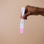 a woman's hand holding a positive pregnancy test on a neutral background.