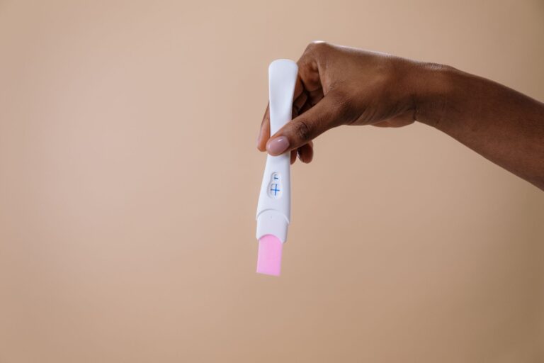 a woman's hand holding a positive pregnancy test on a neutral background.