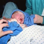 a newborn baby immediately after birth being wrapped in a hospital delivery room.