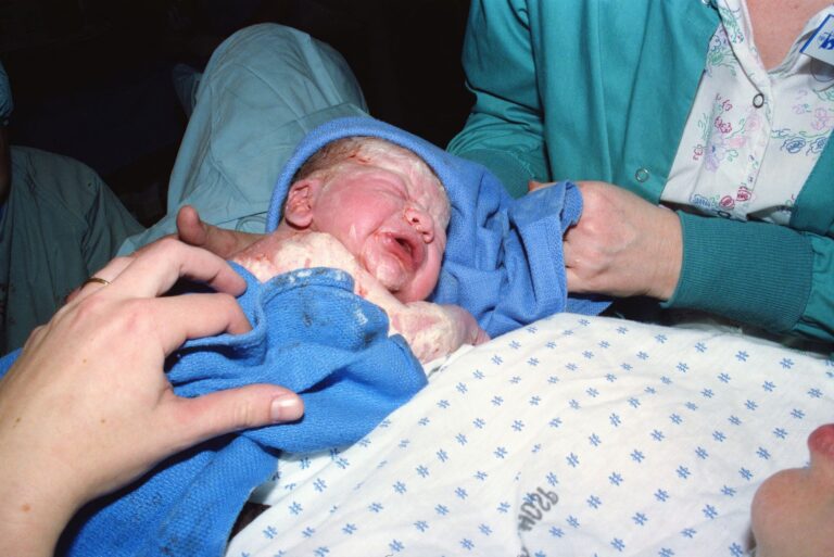 a newborn baby immediately after birth being wrapped in a hospital delivery room.