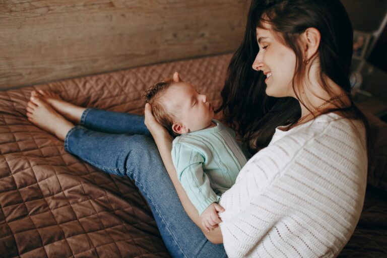 a mother lovingly holds her baby while sitting on a bed, capturing a tender family moment.