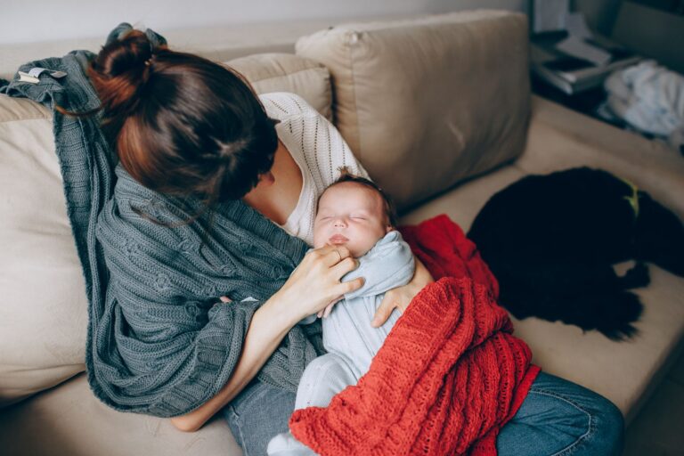 a tender moment of a mother comforting her sleeping baby while resting on a sofa indoors.