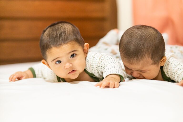 adorable twin babies in matching outfits lying on a cozy bed indoors, capturing a sweet moment.