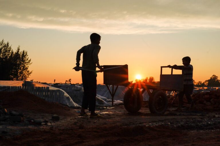 silhouette of kids pushing a wheelbarrow at a construction site during sunset, creating a dramatic scene.