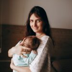 a mother lovingly holds her sleeping baby indoors by a window, capturing a warm and intimate moment.