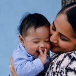 a mother affectionately embraces her baby against a serene blue background.
