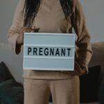 a woman in beige holds a lightbox with 'pregnant' indoors. expectant motherhood concept.