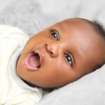 a cheerful baby with open mouth lying on a soft surface, expressing joy and curiosity.