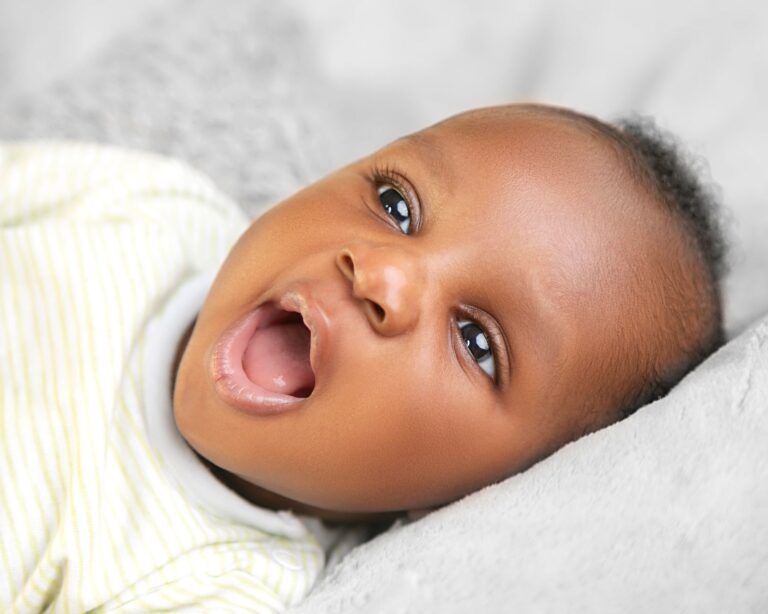 a cheerful baby with open mouth lying on a soft surface, expressing joy and curiosity.