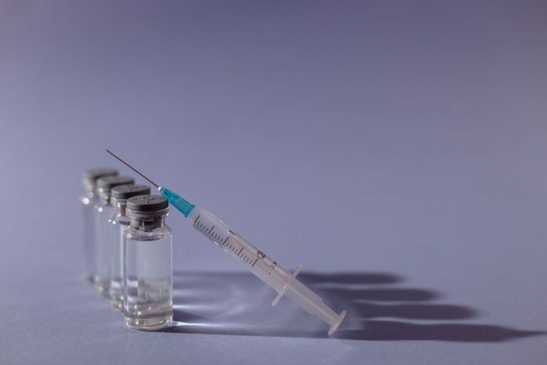 syringe and vaccine vials arranged on gray surface, symbolizing healthcare and immunization.
