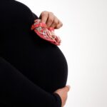 close-up of a pregnant woman holding baby shoes against a white background.