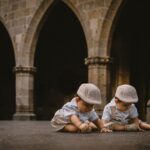 two cute twin boys sitting and playing in a historic courtyard with stone arches.