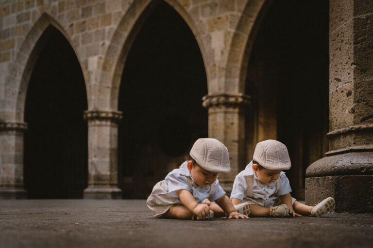 two cute twin boys sitting and playing in a historic courtyard with stone arches.