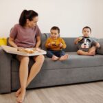 a mother and her twin toddlers enjoying croissants on a sofa, capturing a cozy family moment.