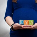 pregnant woman in blue dress holds 'boy' blocks, symbolizing a baby boy announcement.