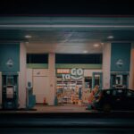 a nighttime view of a gas station and convenience store with a car parked at the pump.