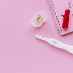 a positive pregnancy test on a pink surface with a pacifier and planner.