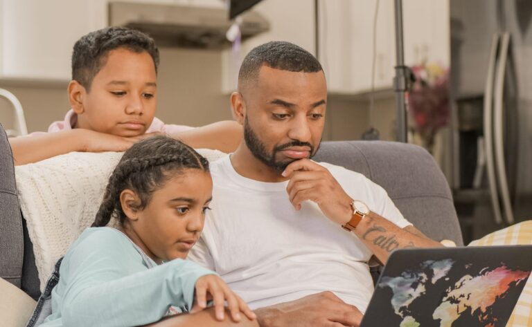 a father and his two children engaged together while using a laptop at home.