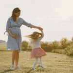 a pregnant mother and her daughter enjoying a joyful moment outdoors in the sunshine.