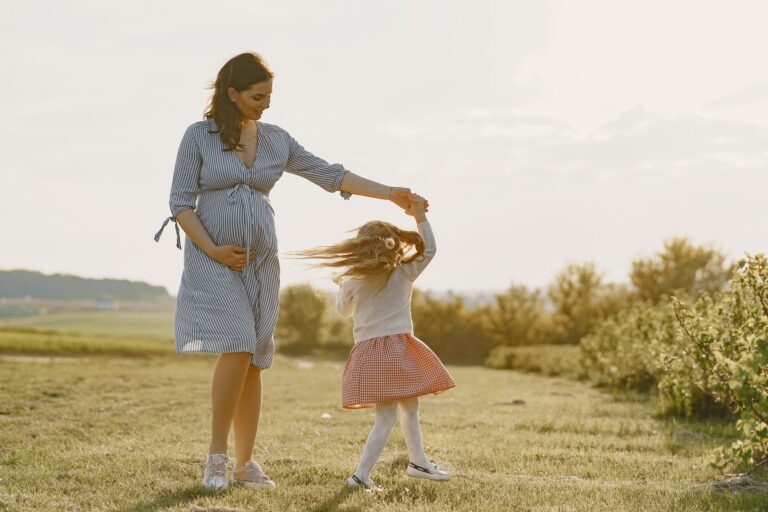 a pregnant mother and her daughter enjoying a joyful moment outdoors in the sunshine.