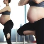pregnant woman doing yoga in front of mirror, promoting health and wellness.