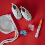 flat lay of baby shoes, pacifiers, hat, and pregnancy test on red surface.