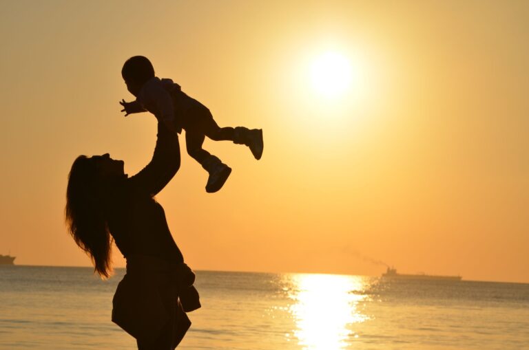 silhouette of a mother lifting her child at a sunset beach, capturing warmth and love.