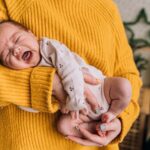 a mother gently holds a crying baby in her arms, providing warmth and comfort indoors.