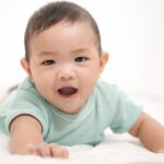 a cute asian baby boy smiling while lying on a white background.