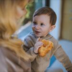 a heartwarming indoor scene of a child enjoying a croissant with their mother.