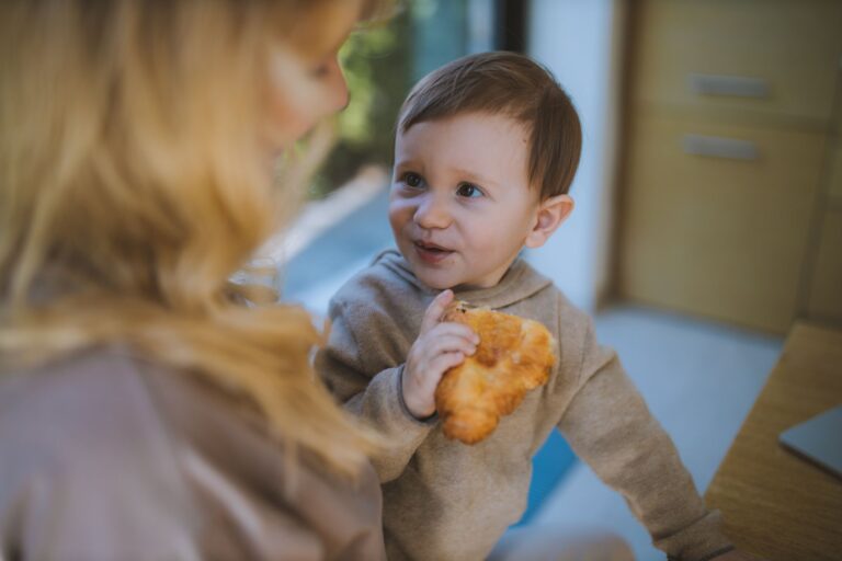 a heartwarming indoor scene of a child enjoying a croissant with their mother.