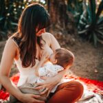 woman breastfeeding baby outdoors on a sunny day, showcasing nurturing and love.