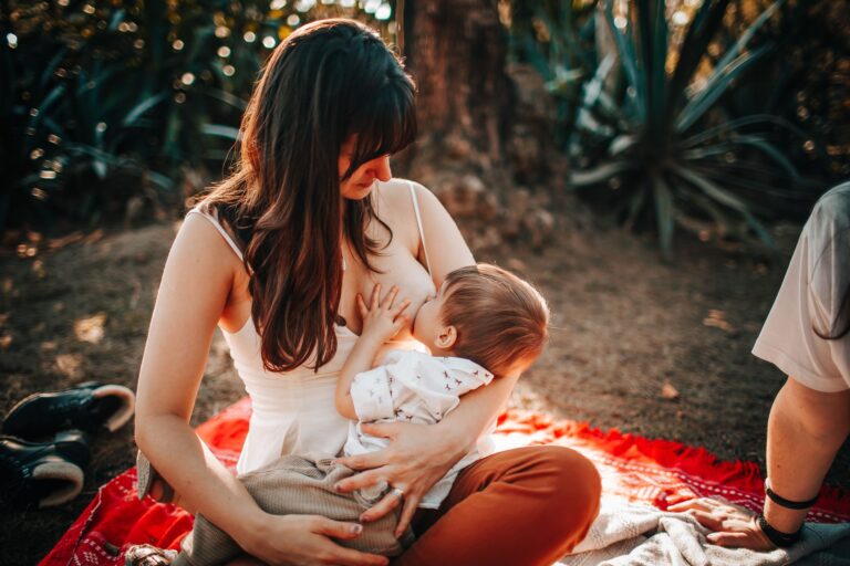 woman breastfeeding baby outdoors on a sunny day, showcasing nurturing and love.