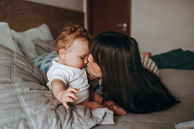 heartwarming moment of a mother kissing her baby in a cozy bedroom setting, symbolizing love and family bonding.