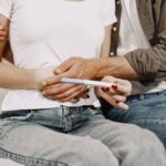 a couple joyfully embraces while holding a positive pregnancy test at home.
