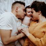 a tender family moment with parents embracing their baby on a cozy bed, symbolizing love and bond.