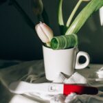 a pregnancy test next to a ceramic mug with tulips, casting dramatic shadows.