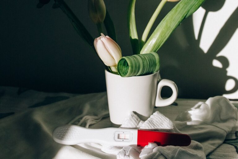 a pregnancy test next to a ceramic mug with tulips, casting dramatic shadows.
