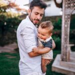 a father lovingly holds his baby in an elegant garden setting, showcasing tender family warmth.