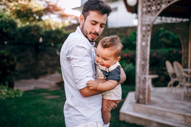 a father lovingly holds his baby in an elegant garden setting, showcasing tender family warmth.