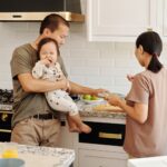a family preparing food in a modern kitchen with a toddler being held by a parent.