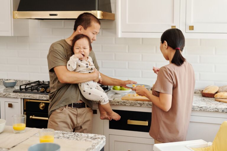 a family preparing food in a modern kitchen with a toddler being held by a parent.
