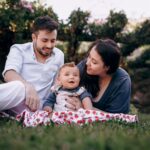 a joyful family bonding with their baby on a picnic in a sunny park.