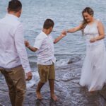 a family dressed in wedding attire enjoying a day at the beach. captured delightfully by the sea.