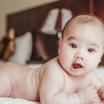 adorable baby lying on a bed, focusing curiously. perfect for parenting and lifestyle themes.