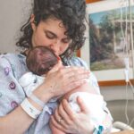mother gently holding newborn baby in hospital setting, showcasing warmth and love.