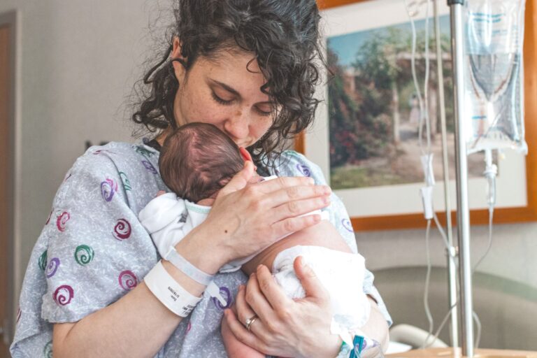 mother gently holding newborn baby in hospital setting, showcasing warmth and love.