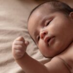 adorable baby lying on a soft beige blanket in natural light.